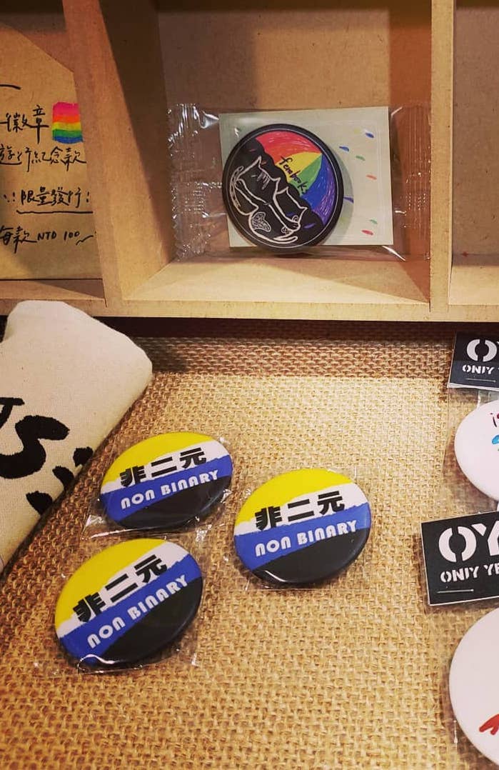various pins on a tabletop, including "nonbinary" written in Mandarin on a nonbinary pride flag