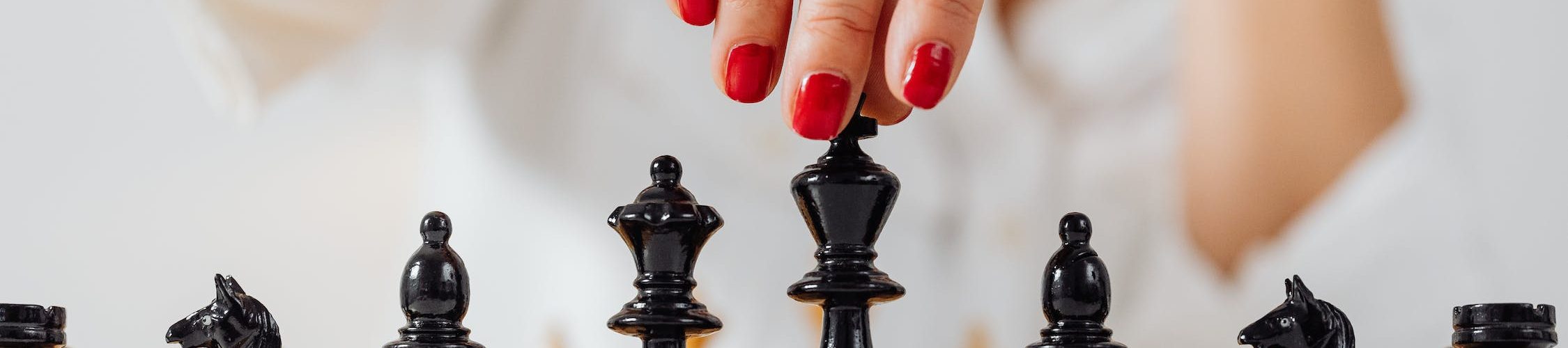 A hand with red nail polish over a chess piece, on a chess board.