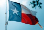 A texas flag flying outdoors, a blue sky in the background